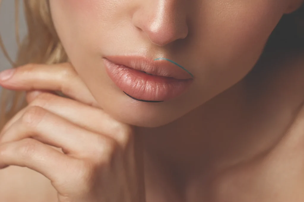 A close-up of a woman's lips and chin, with her hand resting against her face. She has a light complexion and natural makeup.