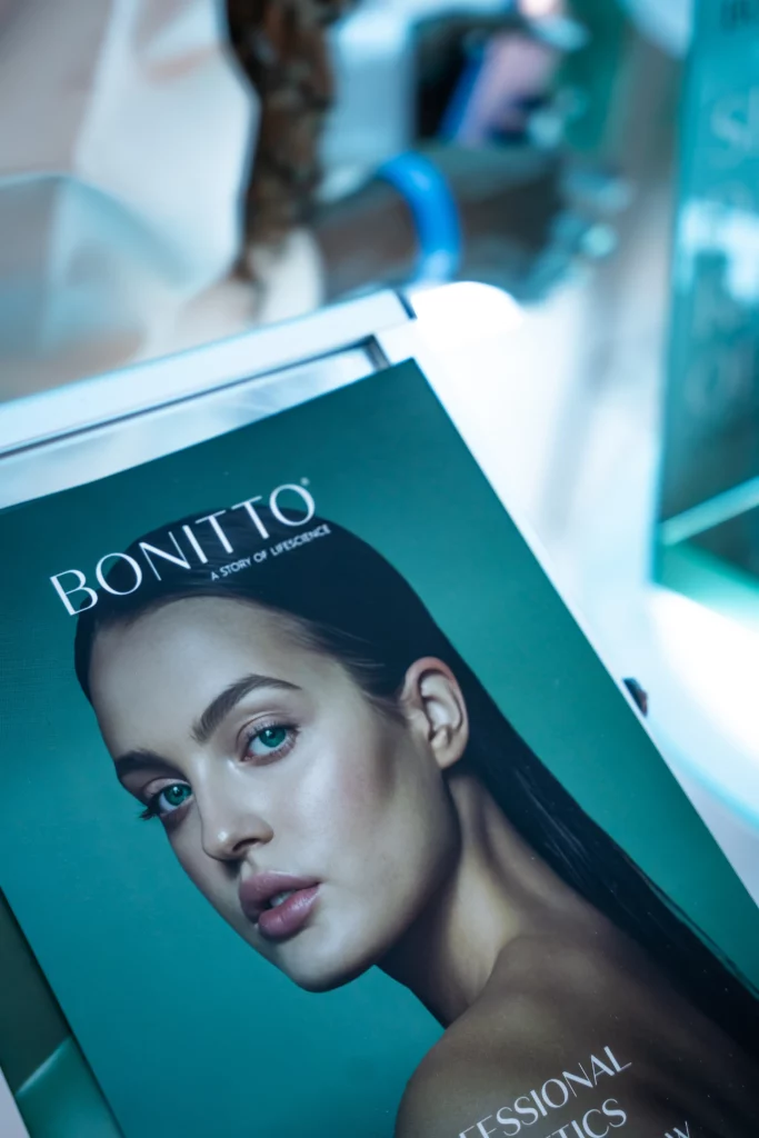 A display features a magazine cover showing a woman with sleek dark hair and glowing skin against a teal background, with the title "BONITTO" at the top and smaller text about professional cosmetics.
