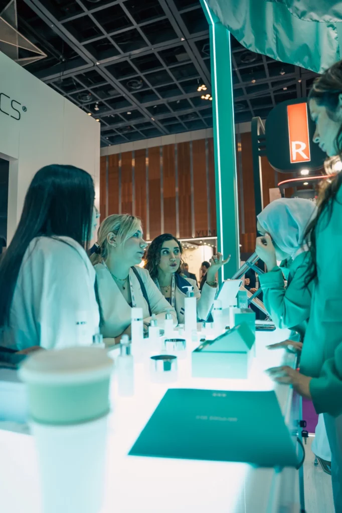 A group of women at a bright, modern cosmetic counter engaged in conversation, with skincare products and brochures displayed on the illuminated tabletop.