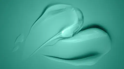 Close-up of a smooth, teal-colored cream or gel smeared in abstract, curved shapes on a matching teal background.