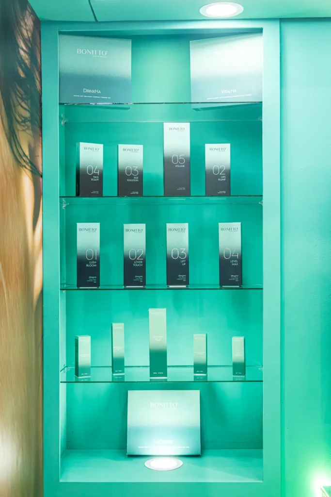 تعرض علبة عرض بلون البط البري عدة صفوف من علب منتجات BONELIQ للعناية بالبشرة، مرتبة بعناية على أرفف زجاجية تحت إضاءة ساطعة.