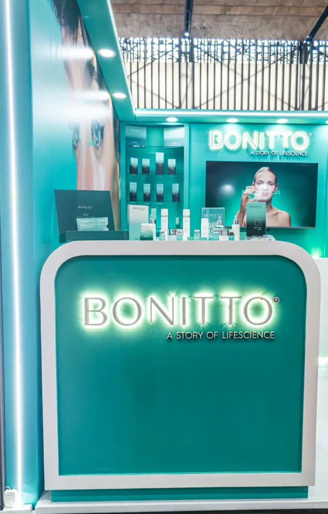 تتميز مقصورة عرض منتجات العناية بالبشرة باللونين الأزرق المخضر والأبيض باسم العلامة التجارية "BONITTO" وشعار "قصة حياة"، مع العديد من منتجات العناية بالبشرة مرتبة بعناية على المنضدة والرفوف.